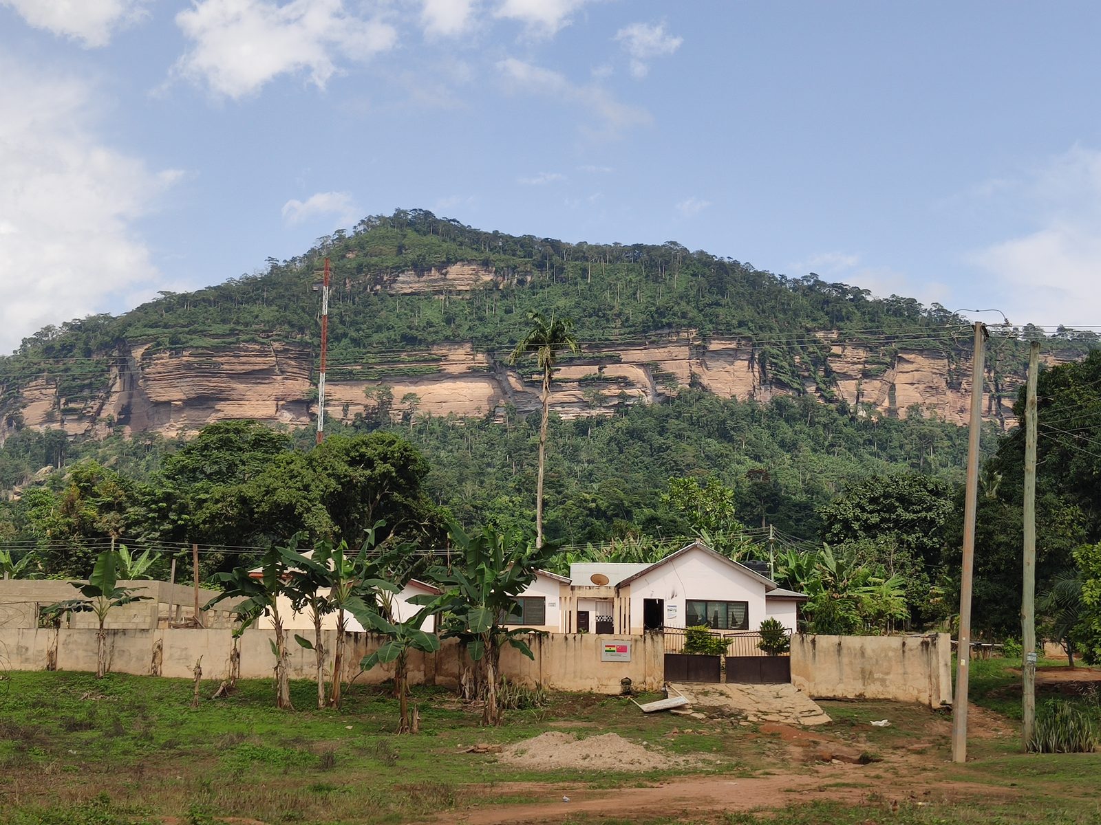 A forested hill with rocky cliffs rising behind a single-storey building.